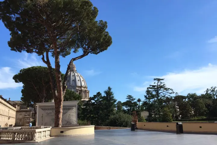 Open plaza with trees and a domed building in the background under a clear blue sky.