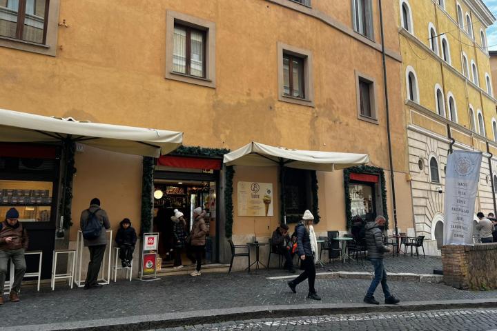 People walking by a cafe with yellow and orange walls, outdoor seating, and awnings.