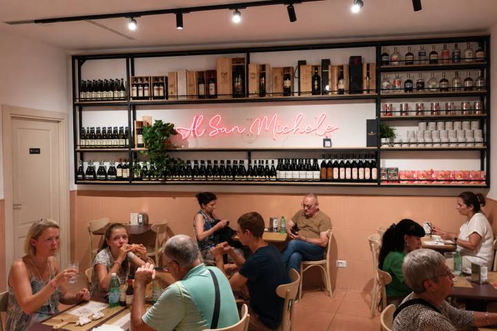People dining in a cozy restaurant with shelves of wine and neon sign.